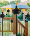 Six Pack 24 Oz Outdoor Garden Torch Set With 55 Inch Citronella Metal Torches And 3 Prong Grounded Stakes in a yard.