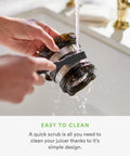 Cleaning the mesh filter of the Nama J2 Cold Press Juicer Hands Free White Self Feeding Hopper under running water.