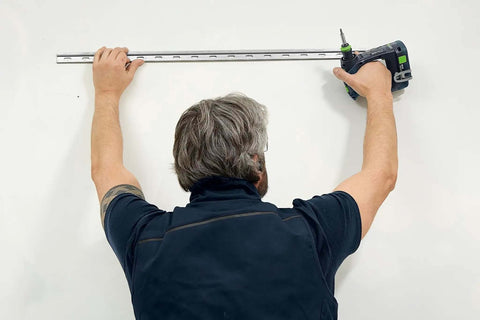 Man using Kickass Cordless Drill Driver Pack Featuring Knockout Torque And Boss Level Brushless Motor to install metal track on wall.