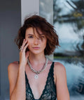 Woman wearing a silver chain necklace with a star pendant, standing outdoors.