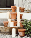Waterproof Outdoor Flameless Pillar Candles 3 Pack In Ivory Resin, 3x4, 3x5, and 3x6 inches on rustic steps with terracotta pots