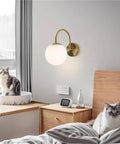 Gold Wall Sconce Mid Century Modern Wall Mount Light Hardwired Sconces Wall Light with Milky White Glass Shade beside cats on bedside.