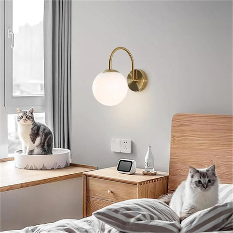 Gold Wall Sconce Mid Century Modern Wall Mount Light Hardwired Sconces Wall Light with Milky White Glass Shade beside cats on bedside.