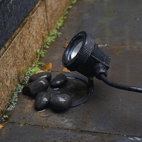 Submersible LED Pond Light Low Voltage Underwater Landscape Lighting for ponds with wet stones in outdoor setting.
