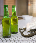 Heavy Duty Cast Iron Mermaid Bottle Opener For Beach House Kitchen Decor, Totally Rad Nautical Bar Essential, Thick Cast Metal Cap Lifter With Killer Coastal Design, Seven Inches next to two green bottles.