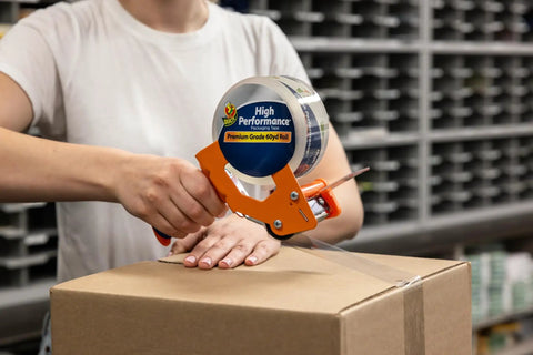 Person using tape dispenser with Six Roll Pack Of High Performance Clear Packing Tape Refills For Shipping Moving Mailing And Storage