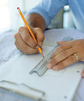Person using Heavy Hitter Yellow Number Two Pencils Presharpened For Butter Smooth Writing on grid paper with a ruler.