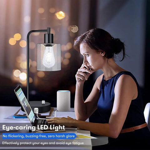 Two Pack Fully Stepless Dimmable Industrial Table Lamps With USB Ports And AC Outlet Seeded Glass Bedside Desk Lamps next to a woman working