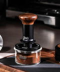 58mm Espresso Tamper With Ripple Base And Spring Loaded Precision Pressure With walnut handle on coffee grounds jar.