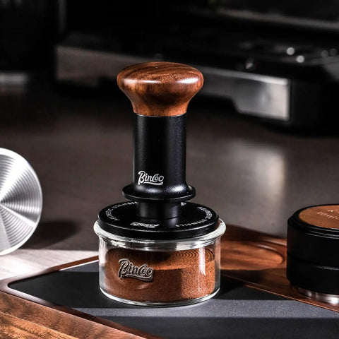 58mm Espresso Tamper With Ripple Base And Spring Loaded Precision Pressure With walnut handle on coffee grounds jar.