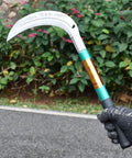 Person holding Heavy Duty Grass Sickle For Weeding And Brush Clearing With Carbon Steel Blade And Iron Handle near plants