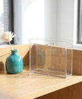 Dual Sided Clear Acrylic Label Roll Dispenser Featuring A Smooth Pull Through Tray Straight Up on a wooden desk beside a small vase.