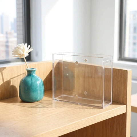 Dual Sided Clear Acrylic Label Roll Dispenser Featuring A Smooth Pull Through Tray Straight Up on a wooden desk beside a small vase.