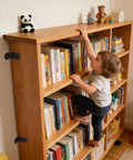 Child climbing bookcase secured with Anti Tip Furniture Anchor Kit For Baby Proofing Dresser And Bookcase, Easy Wall Mount With Two Installation Methods And Safety Straps To Secure Furniture To Wall, Black.