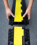 Hands assembling Two Channel Cable Protector Ramp, 3-pack, heavy-duty, yellow and black design for 11000 lbs axle load.