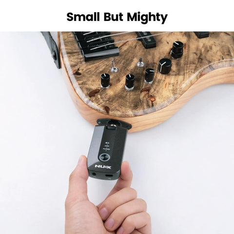 Hand holding Mighty Plug Pro MP3 Guitar And Bass Headphone Amp near a guitar, emphasizing compact size.