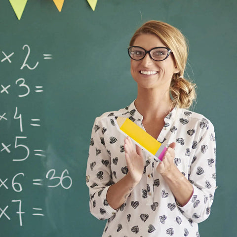 Teacher holding 11 Piece Pencil Name Plates Set For Back To School Blank Wood Desk Signs with chalkboard in the background