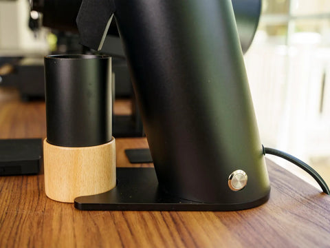 Solid Single Dose Coffee Grinder Featuring 63Mm Red Titanium Conical Burrs And Plasma Ionizer To Crush Beans Sick Flat And Eliminate Static Drama For Flawless Pulls In Sleek Black Housing, side view with wood stand.