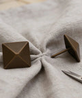 Top Shelf Antiqued Brass Upholstery Nails With Dang Sharp Square Cone Heads Heavy Duty Furniture Tacks Pack Of Thirty on fabric backdrop.