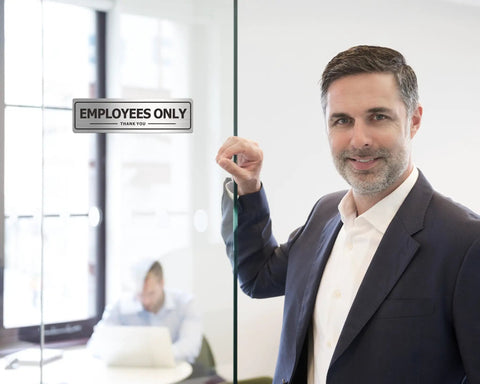 Man standing next to glass door with 'Employees Only' sign, Two Pack Employees Only Door Sign For Office And Business Durable Aluminum Metal Sign With Strong Self Adhesive Weatherproof Indoor Outdoor Brushed Nickel Black Finish Nine By Three Inches visible.