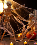 Two Pack 24 Inch Full Body Poseable Skeletons with Locking Joints beside cobwebs and candles for Halloween decor