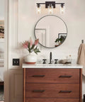 Sleek Matte Black 3 Light Vanity Light With Clear Glass Shades For Bathroom above a modern wood vanity and round mirror