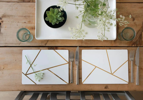 Wooden table setting with geometric-patterned placemats, cutlery, glasses, and a tray with a succulent and flowers.