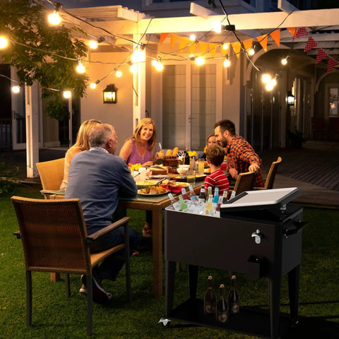 80 Quart Rolling Ice Chest Cart Portable Outdoor Beverage Cooler With Bottle Opener And Cap Collector next to dining table at night