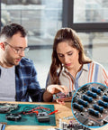Two people working on electronic repairs with a close-up of a 2600-Piece One Quarter Watt Metal Film Resistor Kit With 130 Values From One Ohm To Three Megaohm, One Percent Tolerance, Breadboard Friendly Assortment For DIY Electronics Repairs Projects And Pro Builds.