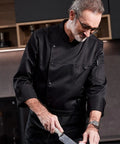 Chef wearing Heavy Duty Chef Coat With Chest And Sleeve Pocket Plus Hella Breathable Fabric That Keeps You Cool In The Heat Top Drawer Restaurant Cook Uniform while chopping.