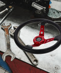 Universal 14 Inch Red PU Racing Steering Wheel With Horn Button on a workshop table with tools.