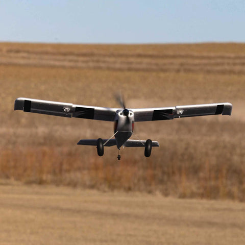RC Airplane Apprentice STOL S 700 RTF With AS3X SAFE Technology flying low over grassy field, white and red color scheme.