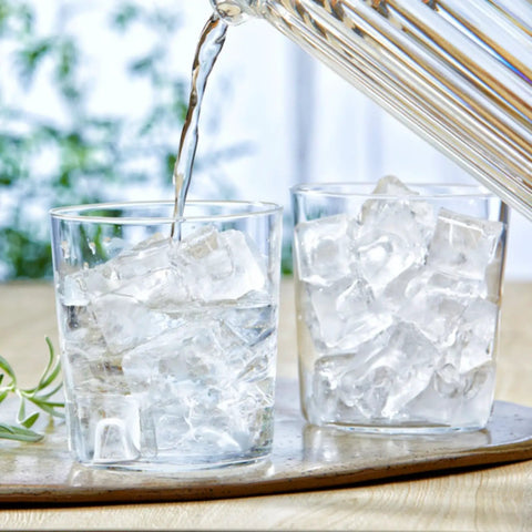 Pouring water into glasses filled with smooth pebble ice near Pro Level Commercial Countertop Nugget Ice Maker.