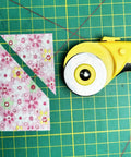 45Mm Rotary Cutter Kit with 9 Extra Blades for Fabric Quilting and Crafting next to cut floral fabric on green grid mat