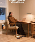 Woman working in home office with Power Saving 450W Space Heater With Remote Wall Outlet Plug As Seen On TV on wall, cat resting nearby.