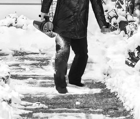 Person using Hand Spreader Shaker For Grass Seed Fertilizer Ice Melt And Snow Salt With Adjustable Openings Up To 80 Oz on snowy path