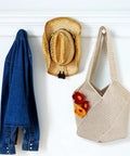 Beige tote bag from Beginner Crochet Bag Kit Complete Starter Set With Yarn, Hooks, Tools And Step By Step Video Tutorials For DIY Tote Bag Crafting Beige Gift For Adults hanging next to hat and denim jacket.