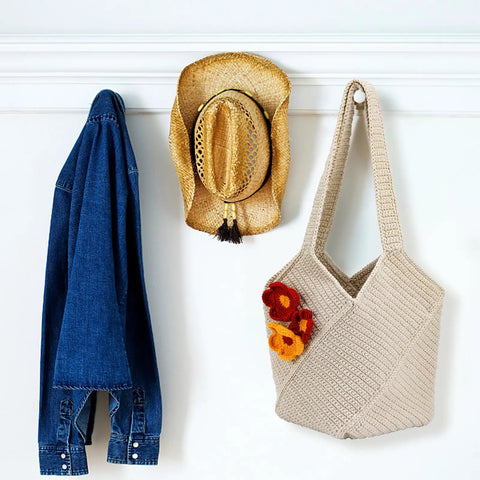 Beige tote bag from Beginner Crochet Bag Kit Complete Starter Set With Yarn, Hooks, Tools And Step By Step Video Tutorials For DIY Tote Bag Crafting Beige Gift For Adults hanging next to hat and denim jacket.