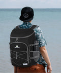 Beast Mode Backpack Cooler Keeps Drinks Ice Cold For Twenty Hours With Hella Leakproof Seals For Hiking Summer Travel Beach Outings Or Weekend Getaways In Durable Black, worn by a person at the beach.