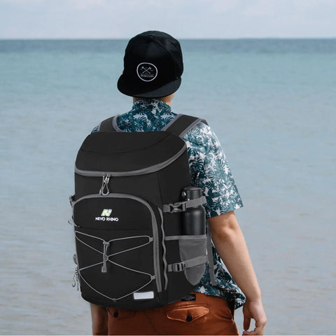 Beast Mode Backpack Cooler Keeps Drinks Ice Cold For Twenty Hours With Hella Leakproof Seals For Hiking Summer Travel Beach Outings Or Weekend Getaways In Durable Black, worn by a person at the beach.