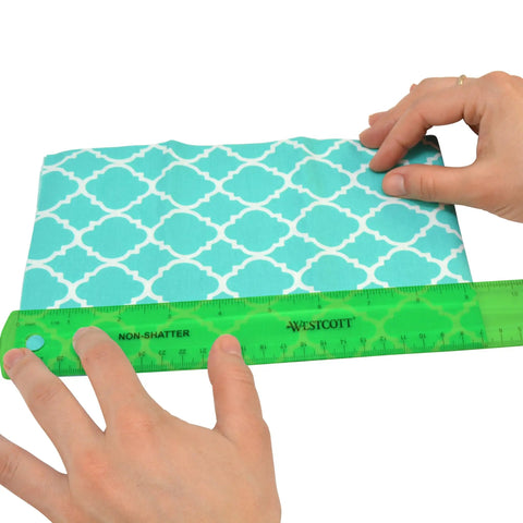 Hands using Shatterproof 12 Inch Ruler In Green With Crystal Clear Markings to measure patterned fabric, shows flexible plastic tool.