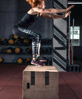 Person performing a box jump exercise in a gym with kettlebells and medicine balls in the background.