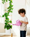 Child watering plant on an extra tall six foot wooden ladder plant trellis for indoor and outdoor garden support easy to install climbing vine trellis for ivy pothos monstera philodendron and other potted plants, showing natural wood sections and lush green vines climbing upward.