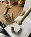 Wooden articulated hand model on a workbench with woodworking tools in the background, viewed from above.