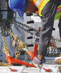Worker securing load with Grade 70 Three By Eight Inch Chain And Binder Kit, showing two chains and two binders on flatbed.