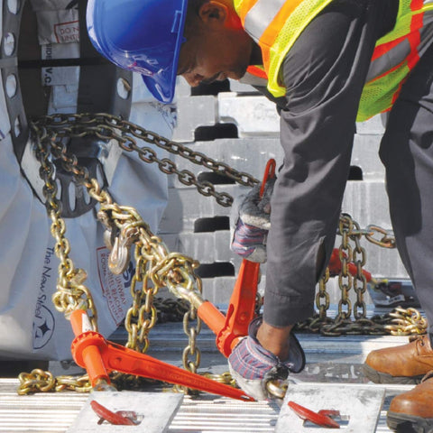 Worker securing load with Grade 70 Three By Eight Inch Chain And Binder Kit, showing two chains and two binders on flatbed.
