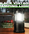 Black vintage LED lantern glowing on a table, part of Collapsible Camping Lantern 4 Pack Battery Operated LED Super Bright Light.