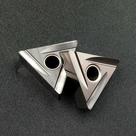 Two triangular ceramic TNMG cutting inserts with center mounting holes for lathe turning