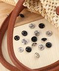 100 Sets Of 10 mm Sew On Snap Buttons For Clothing Metal Snaps Fasteners Press Studs In Black And White Durable Garment Snaps For Sewing Projects Sweet For DIY Garment Crafts And Repairs scattered on wooden surface near fabric and leather strap.