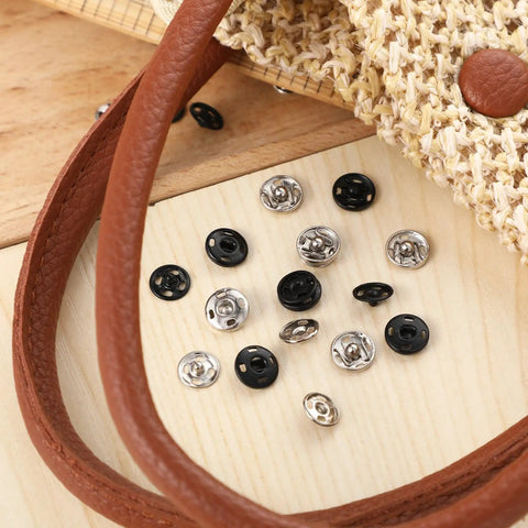 100 Sets Of 10 mm Sew On Snap Buttons For Clothing Metal Snaps Fasteners Press Studs In Black And White Durable Garment Snaps For Sewing Projects Sweet For DIY Garment Crafts And Repairs scattered on wooden surface near fabric and leather strap.